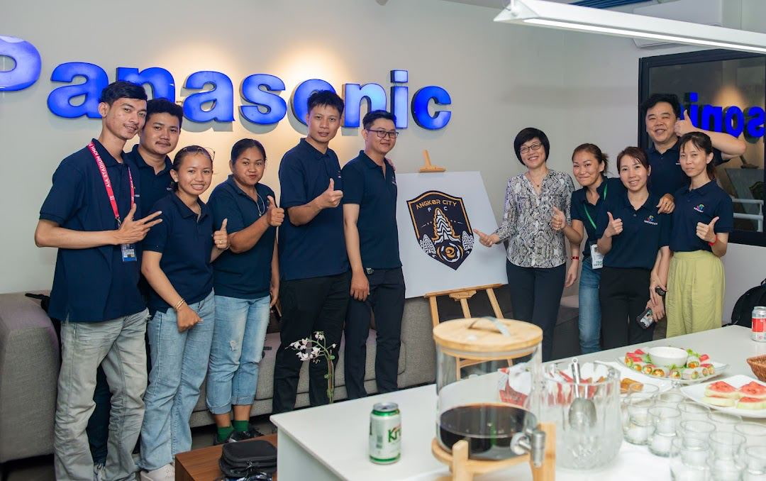 WeWatch team standing in front of Angkor City FC poster
